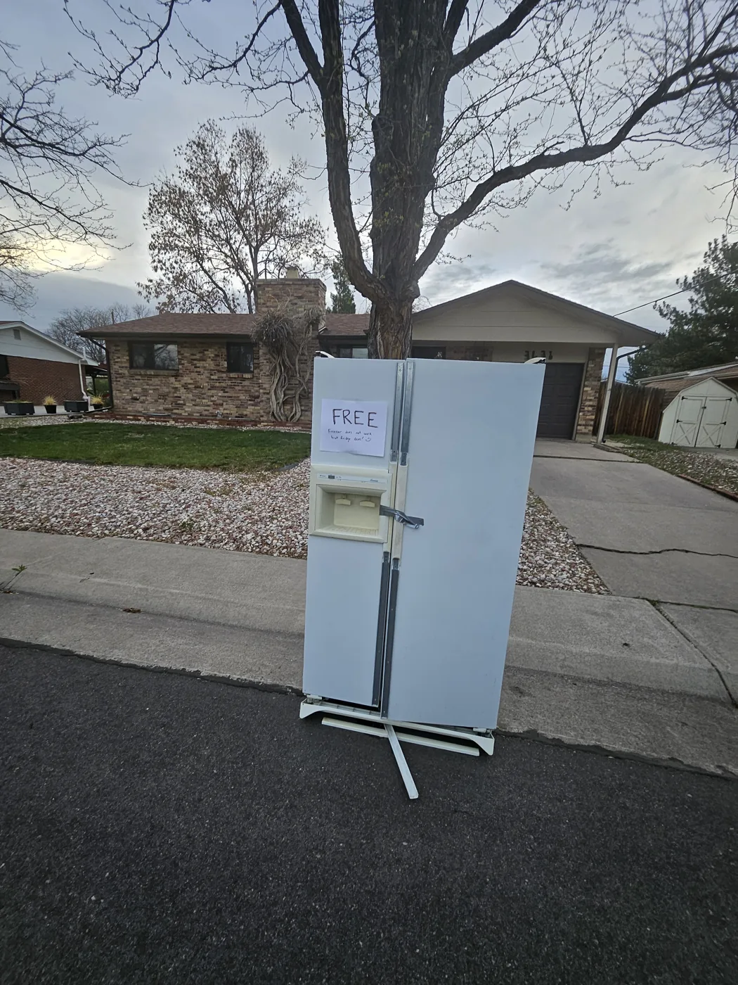 A side-by-side refrigerator left at the curb with a handwritten FREE sign — the kind of appliance city curbside won't haul away